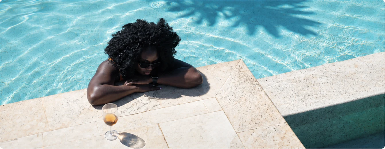 A traveller relaxing beside turquoise pool water with a drink on the stone terrace